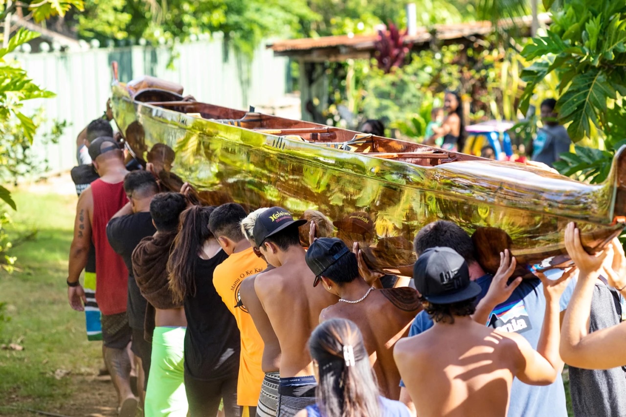 An ohana lifting a koa canoe together